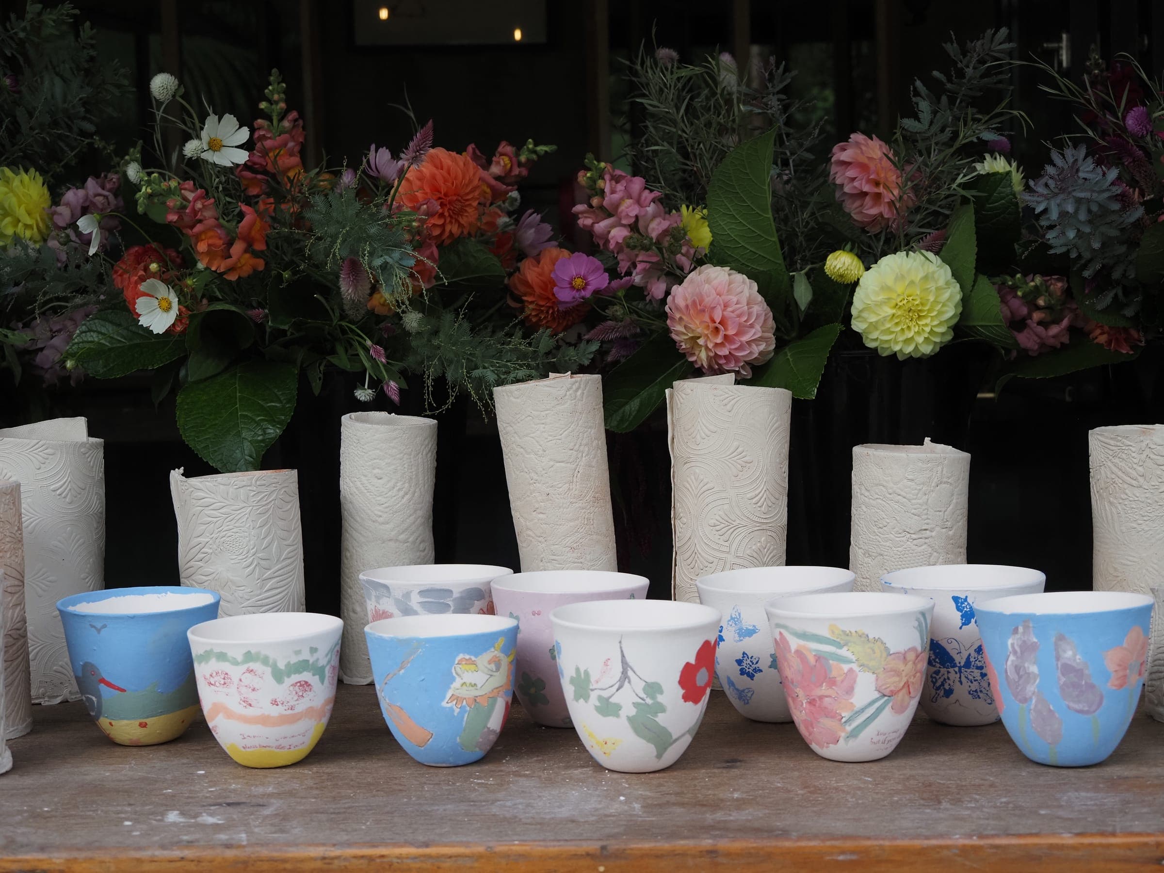 Painted cups and tall white vases filled with fresh garden flowers