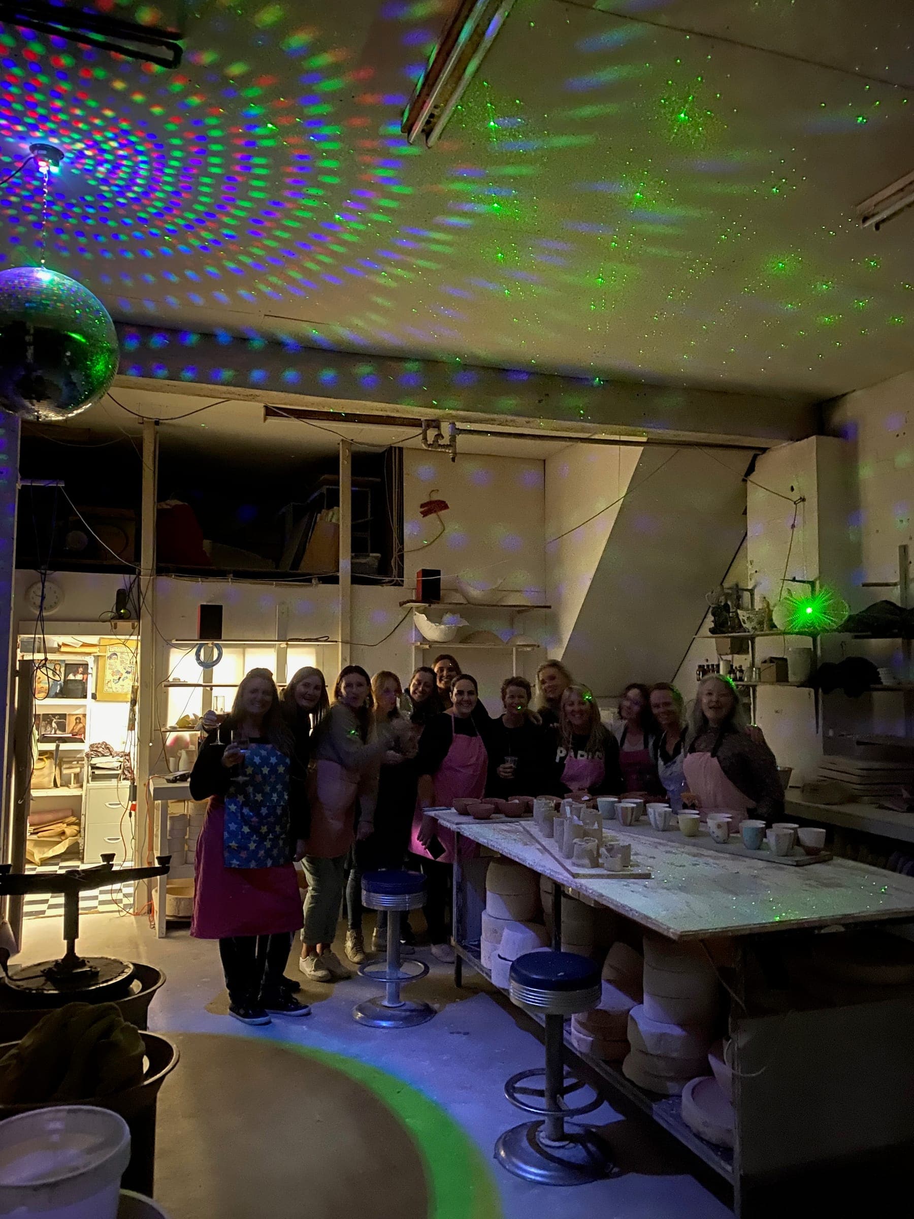 A crowd of makers in pink aprons posing under scattered disco lights in the studio