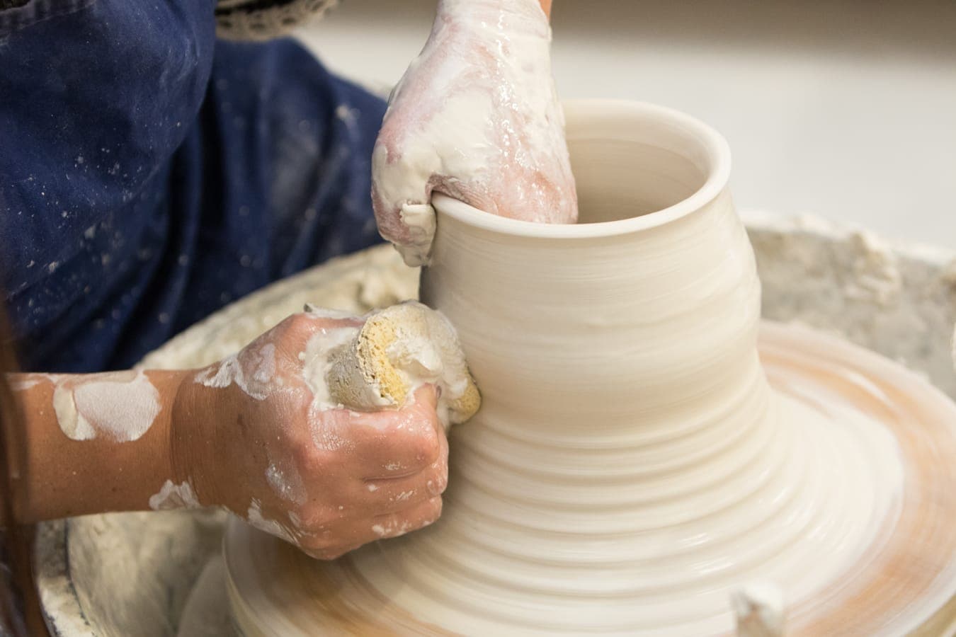 Clay-covered hands pulling up the wall of a pot on the wheel