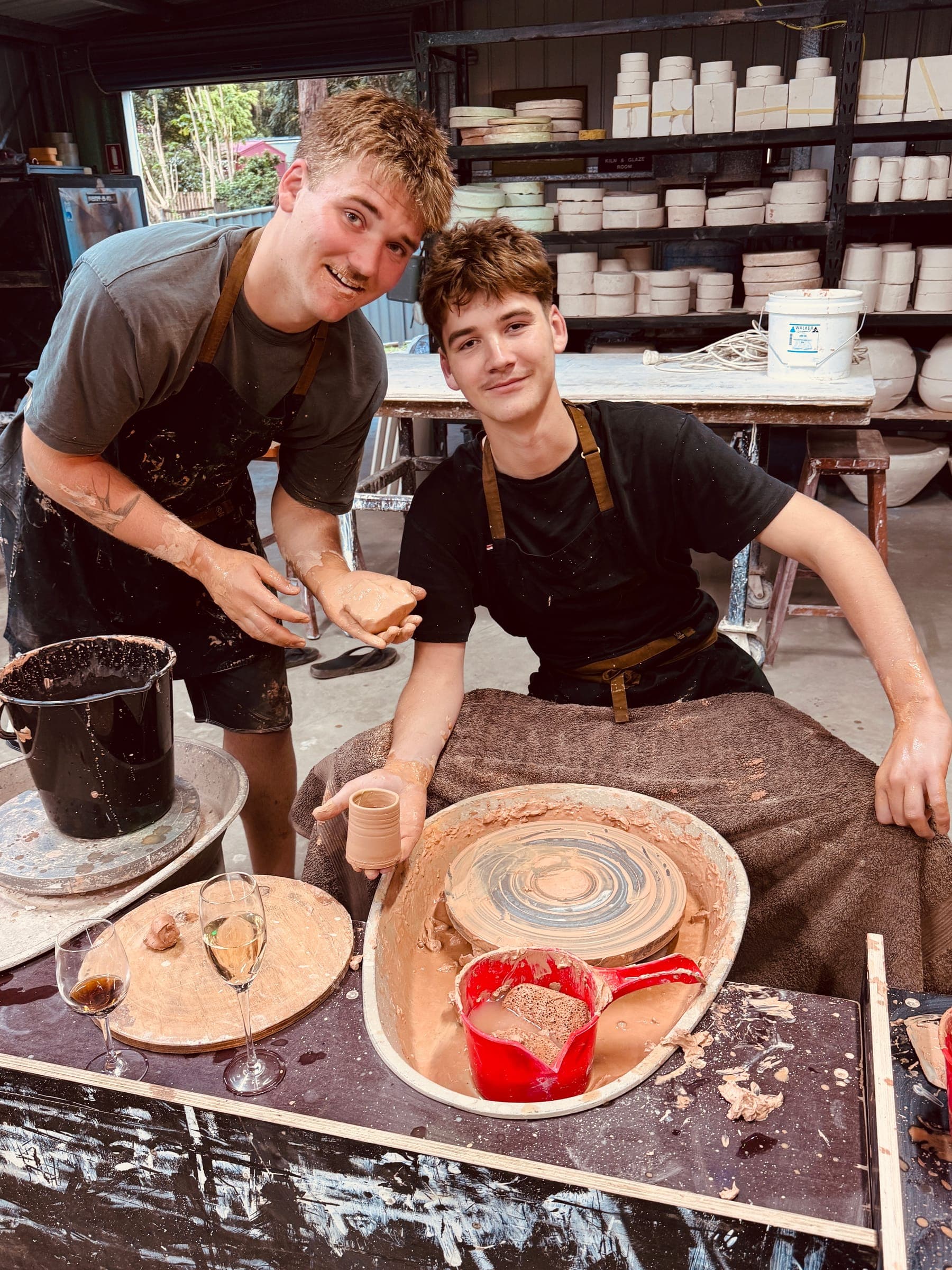 Jack and Charlie grinning over their wheels, aprons covered in slip